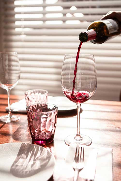 red wine being poured from a wine bottle into a stemmed wine glass on a table