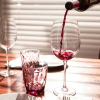 red wine being poured from a wine bottle into a stemmed wine glass on a table